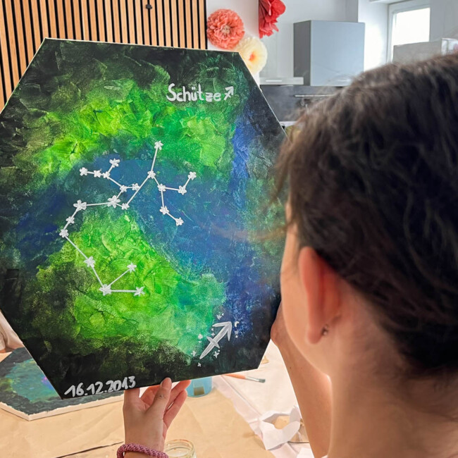 Malkurs Kinder Köln - Kind zeigt stolz eine Leinwand mit selbstgemalter Sternzeichen-Galaxie.