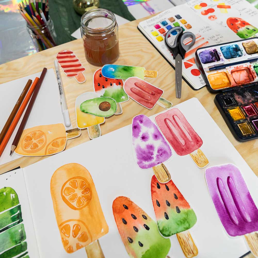 Bunte Aquarellbilder mit Eis- und Wassermelonenmotiven sowie Farben und Pinseln bei einem Aquarell Workshop für Kinder im MrsBerry Studio bei Köln.