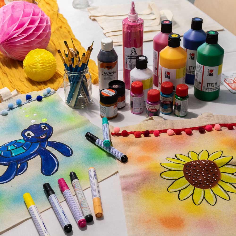 Bemalte Stoffbeutel mit Schildkröte und Sonnenblume sowie bunte Textilfarben bei einem kreativen Kindergeburtstag im MrsBerry Studio bei Köln.