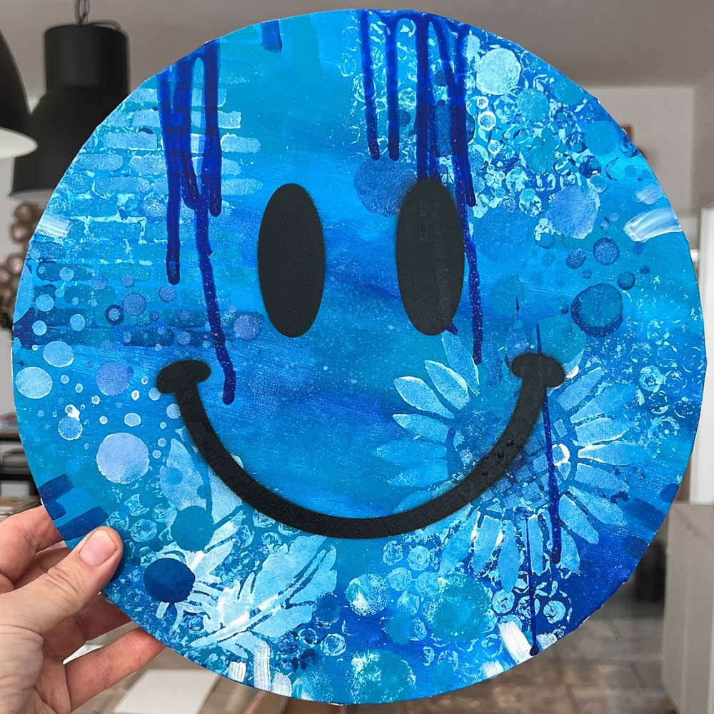happy-face-art-blau-runde-leinwand-workshop-koeln Hochgehaltenes Happy Face Art in verschiedenen Blautönen auf runder Leinwand