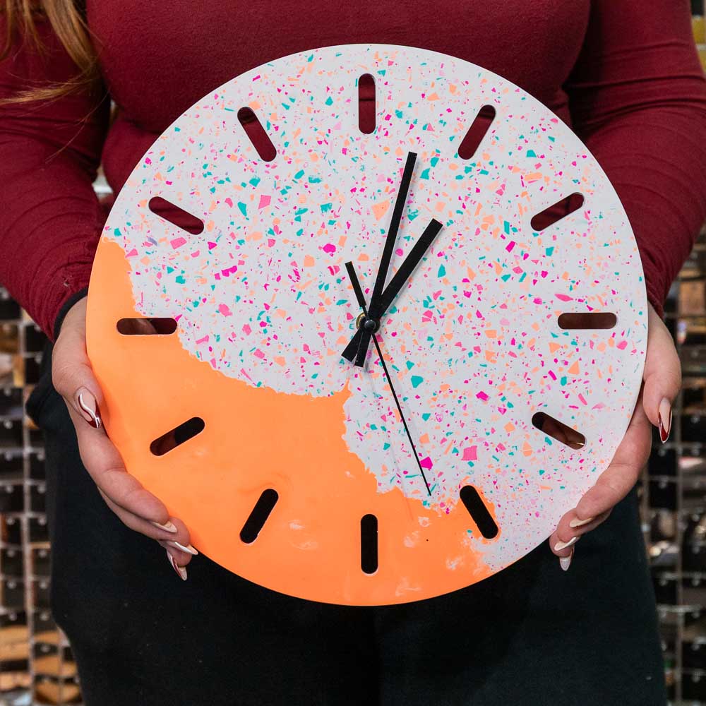 Teilnehmerin hält eine selbst gegossene Uhr in Neonfarben mit Terrazzo-Elementen aus dem Uhr Spezial Workshop
