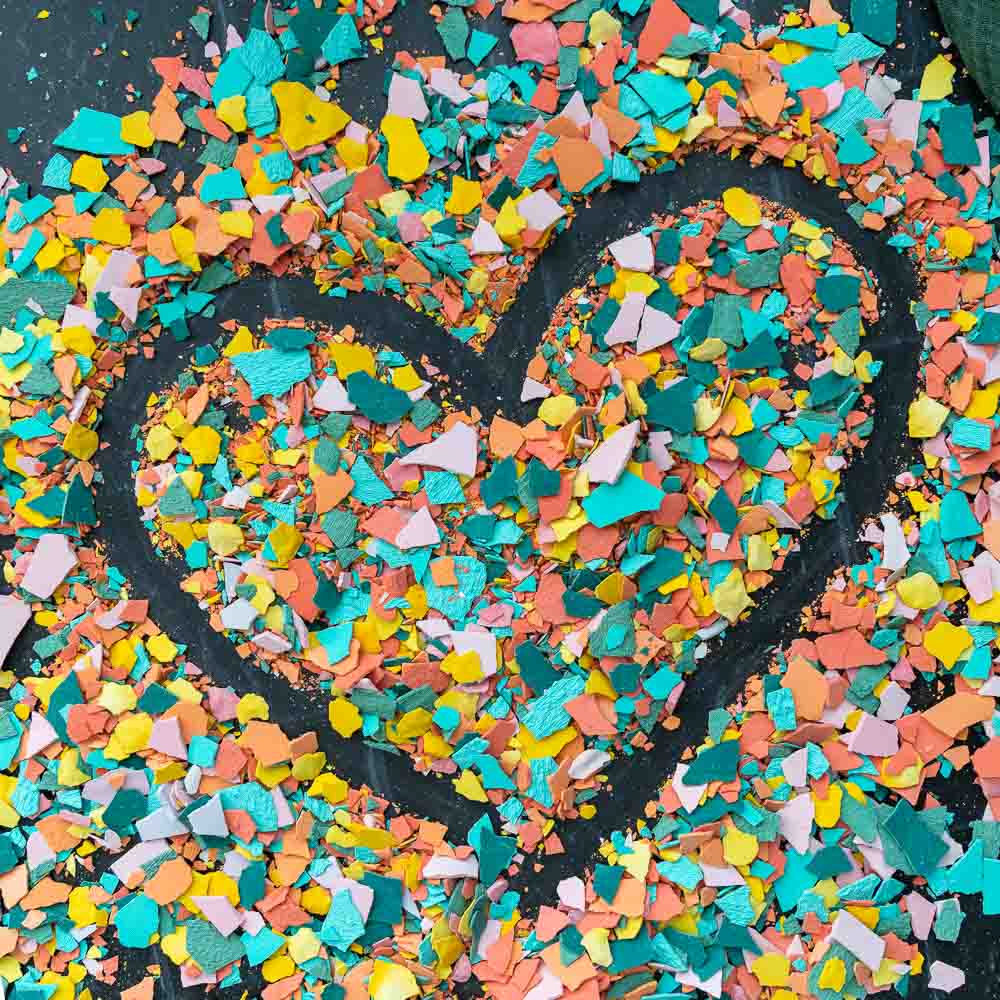 Bunte Terrazzo-Chips aus Gießpulver auf einem Tisch, mit den Fingern zu einer Herzform geschoben